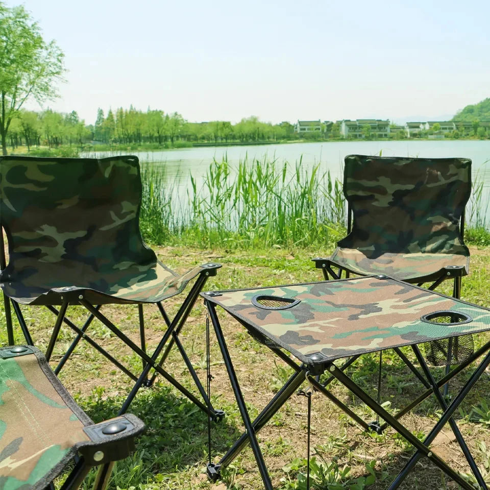 Camouflage chairs and table set up by a lake with greenery.
