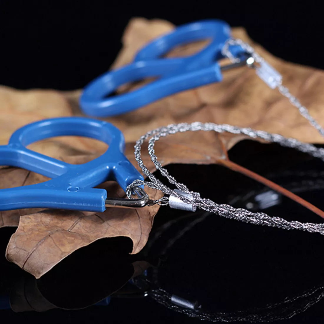 Blue and silver tactical saw on a dark surface with leaves